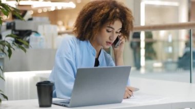 Afrikalı Amerikalı kız öğrenci kıvırcık iş kadını birden fazla iş yapan kadın yönetici danışmanı telefonla konuşuyor dizüstü bilgisayarla yazı yazıyor notlar yazıyor internetteki uzaktan görüşmeler üzerinde çalışıyor.