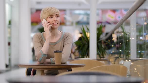 Caucásica madura adulta de mediana edad de 40 años mujer de negocios sentada en la mesa en la cafetería hablando en el teléfono móvil teléfono inteligente contestando llamada orden en línea negociación remota conversación distante comunicación — Vídeos de Stock