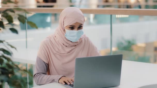Здивована арабська жінка в медичній масці дивиться на екран ноутбука, отримуючи електронну пошту, читаючи хороші новини, святкуючи успіх перемоги, радіючи перемозі в лотереї, отримуючи приз просування нової кар'єри — стокове відео