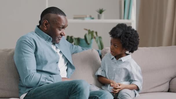 성숙 한 흑인 미국 남자 소파에 앉아 아기 여자 아이와 이야기를 하는 사랑 스런 아버지는 어린 딸에게 그녀가 학교에서 보낸 여가 시간 이 어떻게 가족 과좋은 대화를 하는지 묻는다. — 비디오
