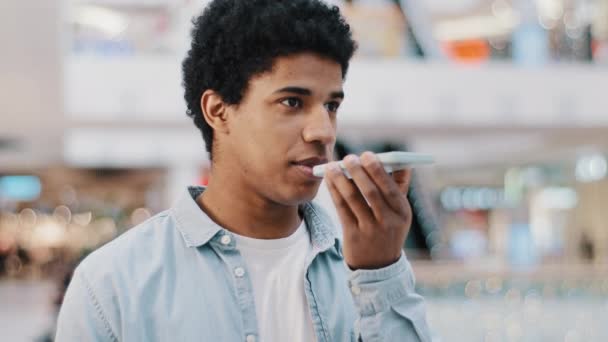 Hombre afroamericano grabando mensaje de reconocimiento de voz en altavoz en interiores. Chico usando asistente virtual conjuntos de aplicaciones recordatorio en el teléfono móvil dicta palabras. Concepto tecnológico de asistencia móvil digital — Vídeos de Stock