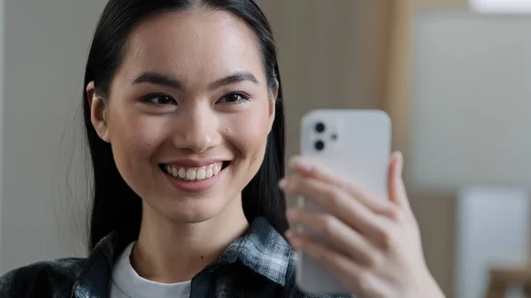 Happy asian korean Japanese Chinese girl smiling female face woman with mobile phone waving hand talking to webcam make video call at home talking chatting by virtual video call app online meeting — Stock Photo, Image