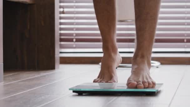 Close-up pernas masculinas esbelto fino desportivo irreconhecível cara atleta masculino em pé em casa banheiro andando descalço em balanças eletrônicas verificando emagrecimento controle do corpo quilogramas esportes engorda — Vídeo de Stock