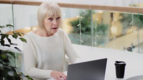 Excitada mulher caucasiana de meia-idade animado sentado na mesa usando laptop intensamente jogar jogo de computador ganhando prêmio em dinheiro na loteria casino online em leilão celebrando vitória vitória vitória sucesso — Vídeo de Stock