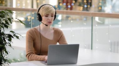 Orta yaşlı, 40 'lı yaşlarda, mikrofonlu bir iş kadını laptop web kamerası danışmanlığında uzaktan öğretmen koçu yardım hattı yöneticisi danışmanı video konferansında sohbet etmeyi tavsiye ediyor.