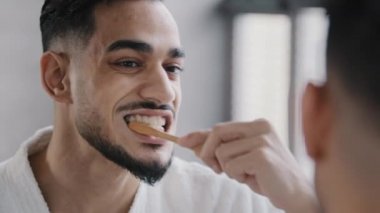 Yakın plan erkek yansıması aynada sakallı bir adam diş fırçasıyla beyaz diş macunu ile dişlerini fırçalıyor ev banyosunda günlük temizlik konseptinde diş fırçası temizliyor.