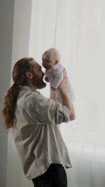 Dikey bir bakış açısı beyaz sakallı baba yeni doğmuş bebeği kucağında tutuyor babası bebek gıdıklayan çocukla burun buruna dokunuyor eğleniyor kız çocuğunu oğluyla bağ kuruyor
