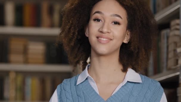 Närbild söt ung afrikansk amerikansk flicka tonåring stående i biblioteket tittar på kameran poserar leende kvinnlig porträtt student läroanstalt högre utbildning koncept vid universitet eller högskola — Stockvideo