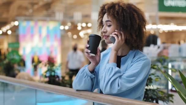 Vrouwelijk Afrikaans Amerikaans zakenvrouw praten telefoon op afstand vriendelijk gesprek bellen online boeking maken orde met smartphone meisje drinken thee koffie in winkelcentrum bedrijf mobiele tech praten — Stockvideo