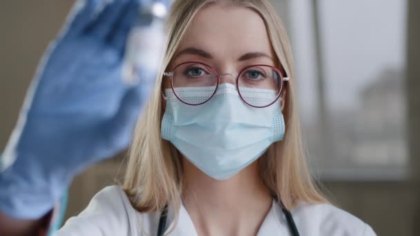 Κοντινό πλάνο γυναίκα ειδικός χημικός βιοχημικός γυναίκα γιατρός νοσοκόμα επιστήμονας σε ιατρικά γυαλιά μάσκα και γάντια λατέξ κοιτάζοντας κάμερα κρατώντας μπουκάλι του εμβολίου covid coronavirus έννοια εμβολιασμού — Αρχείο Βίντεο