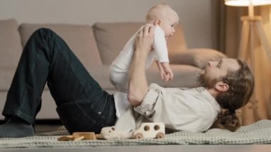 Evde beyaz bir aile, yetişkin, sakallı bir baba, yerde küçük kızıyla birlikte uzanmış, bebek bebekle oynuyor, yeni doğmuş bebeklerle konuşuyor, birlikte vakit geçiriyorlar, bakıcı babalık kavramını benimsiyorlar.