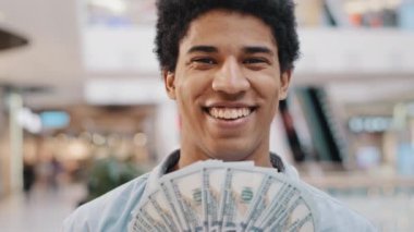 Mutlu, zengin, başarılı, gülümseyen Afrikalı Amerikalı iş adamı elinde para fanı tutarken dolar banknotlarının arkasına saklanıyor ve maaş tasarrufu kredisi aldığını gösteriyor.
