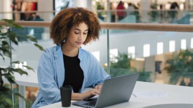 Afrika kökenli Amerikalı öğrenci kız milenyum iş kadını kadın serbest çalışan kullanıcı yöneticisi kafeteryada oturmuş kahve içiyor dizüstü bilgisayarla çalışıyor internetten internete girip interneti kuruyor.