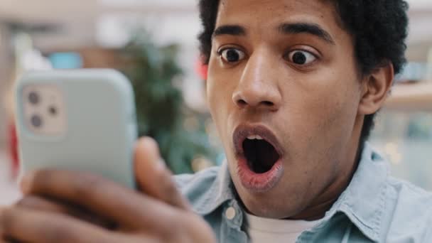 Detailní záběr portrét šokován Afroameričan tisíciletý muž otevřených úst v šoku při pohledu na obrazovce smartphone pocit údivu strach se špatnou neočekávané zprávy selhání vyhozen z práce chlap se dívá na telefon — Stock video
