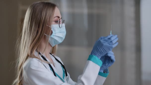 얼굴에 마스크를 쓰고 의료 가운을 입고 주사를 맞을 주사기를 준비하고 있는 여성 의사. 액체 의약품 항생제 항바이러스제 백신 백신을 가지고 있는 여성 간호사 바이러스 예방 — 비디오