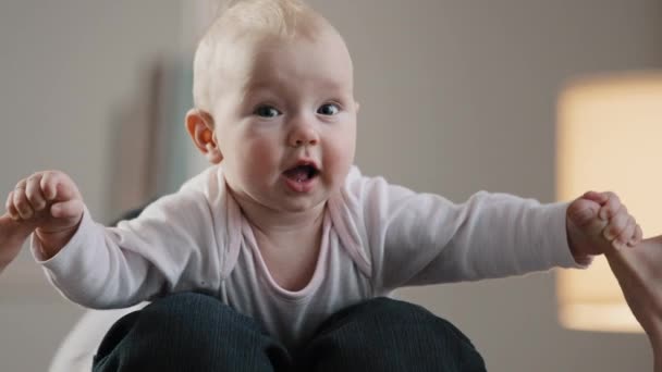 Närbild oigenkännlig pappa håller baby på knä ben leka flygplan spel med spädbarn låtsas flyga hemma njuta av faderskap barndom nyfödda leende visar tunga tittar på kameran — Stockvideo