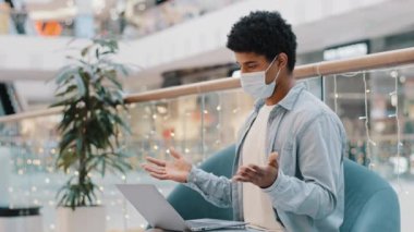 Yüzü tıbbi maske takan Afrikalı bir adam. İş yeri videosu. Laptop salgını online öğretmen özel hocası uzaktan sohbet eden internet konferansı Webinar 'ı konuşuyor.