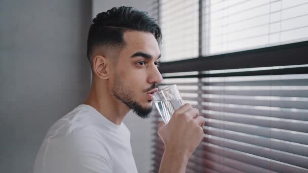 Іспанська індійська арабська бородатий хлопець тисячолітній чоловік дивиться вікно вдома в спортзалі п'є чисту смачну воду з прозорого скла, що зволожує спрагу концепції балансу охорони здоров'я щоденна звичка — стокове відео