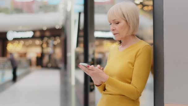 Lächelnde ältere kaukasische Frau mittleren Alters, die ihr Handy auf den Smartphone-Bildschirm hält und E-Mail-Nachrichten mit mobiler Anwendung sendet, die in sozialen Medien im Online-Shop einkauft — Stockvideo