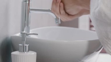 Banyo bornozlu tanınmayan genç adam yakın çekim erkek elleri, el yıkama için sıvı sabun çevre dostu ürün jeli, otel tuvaletinde el yıkama, günlük hijyen vücut bakımı konsepti.