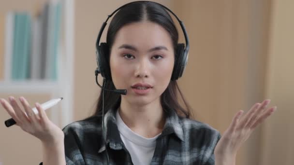 Webbkamera visa asiatisk kvinna arbetsledare kvinnlig koreansk agent hjälp linje konsult flicka bär headset huvud mikrofon talar råder förklarar visar i luft gest kundsupport operatör — Stockvideo