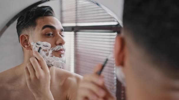 Hispânico árabe árabe indiano barbudo homem bonito barbear usando lâmina descartável no banheiro olhando para o espelho. Procedimento diário de beleza higiênica masculina de rotina matinal. Guy barba barba e bigode — Vídeo de Stock
