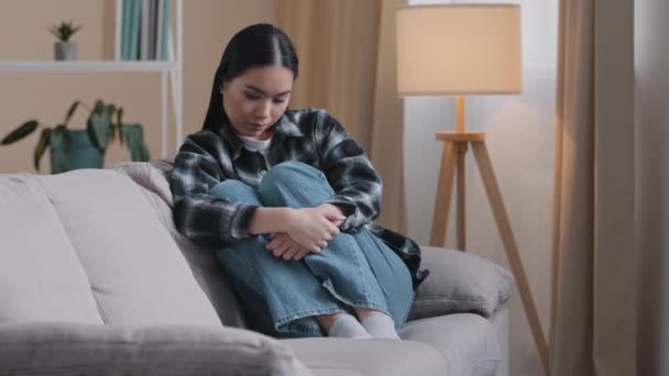 忧心忡忡的亚裔韩国女人有心理问题坐在沙发上感到孤独焦虑不安沮丧的日本女孩因家庭悲伤而沮丧困扰着意外怀孕的厌倦 — 图库视频影像
