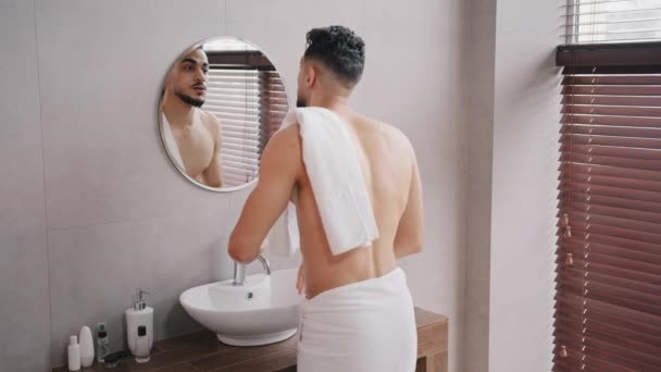 Nagi arabski arabski arabski indyjski brodaty człowiek mycie twarzy patrząc w lustro wycieranie mokry twarz z biały ręcznik facet rano prysznic skóra pielęgnacja rutyna przygotowuje się w łazienka mężczyzna piękno skóra pielęgnacja mycie twarzy — Wideo stockowe