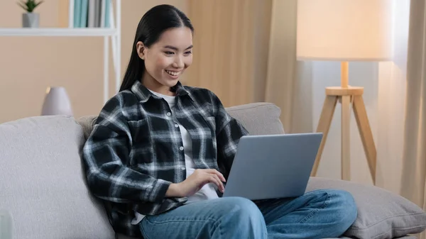 Asiatique 20s fille utilisateur millénaire femme étudiante pigiste chat internet avec ordinateur portable canapé maison jouer jeu d'ordinateur sourire heureux de choisir le shopping regarder la vidéo drôle réseaux sociaux app — Photo