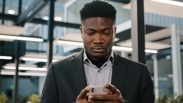 Serious young man african american office worker looking smartphone internet choose making order chatting online with friends scrolling mobile phone thoughtful male user cliquez sur le compte du navigateur — Photo