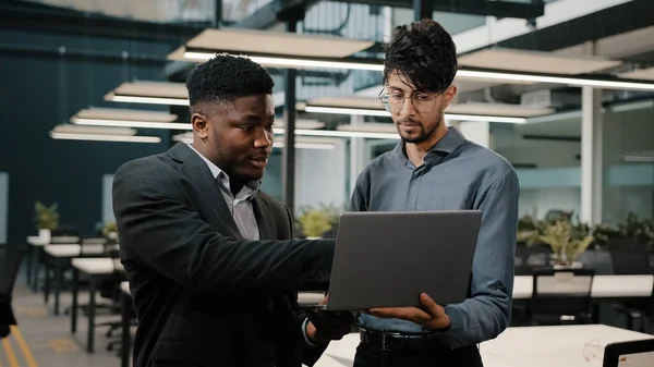 Två manliga affärspartners män Arabian man håller laptop visar presentation Afrikansk affärsman tittar på datorskärm kollegor som arbetar online diskutera start pekskärm gör val — Stockfoto