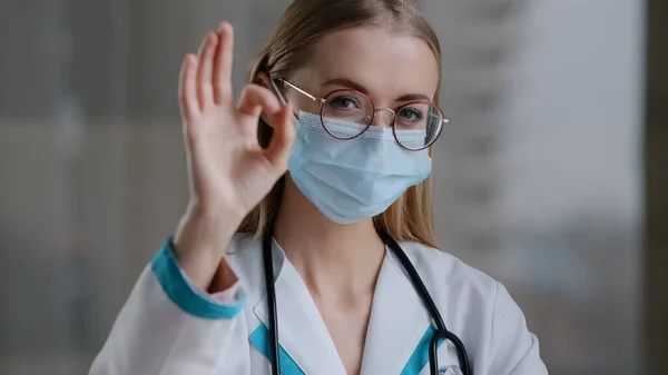Portré kaukázusi orvos szakorvos terapeuta sebész nő lány szemüvegben orvosi védő arc maszk nézi a kamera mutatja ok gesztus kiváló tökéletes finom jól jó siker jele — Stock Fotó