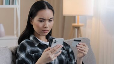 Öfkeli Asyalı kadın evinde kanepesinde oturuyor kredi kartı kullanıyor cep telefonu kullanıyor e-banka başvuru ödeme ödemeleri ile ödeme yapmaya çalışıyor bankacılık hatası yok para çevrimiçi mali işlem başarısız