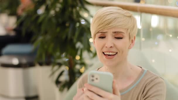 ヘッドショットポートレート白人中年40代女性モバイルアプリユーザーショートヘア女性は電話で見て戦争の良いニュースを読み取りますメッセージを取得しますゲームはい手ジェスチャーの勝利の成功を作ります — ストック動画