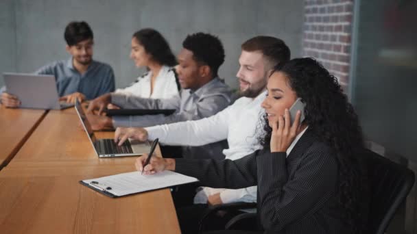 Diversi dipendenti seduti in ufficio donna d'affari ispanica che parla al telefono con i clienti conducono consultazioni colleghi gioiosi che lavorano a un progetto congiunto utilizzando tecnologie moderne sul posto di lavoro aziendale — Video Stock