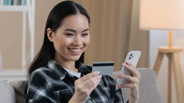 Gülümseyen Asyalı etnik kadın müşteri kullanıcısı evde akıllı telefon yazan sanal parayla banka kartı tutuyor. İnternetten satın almak için mobil ödeme uygulaması kullanan çok ırklı mutlu bayan müşteriler. — Stok fotoğraf