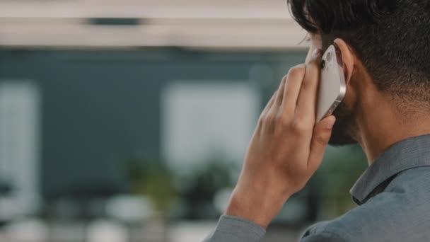 Vista posterior del exitoso comerciante indio árabe inversor haciendo llamada hablando en la oficina disfrutando de la conversación móvil en el interior comunicarse con la pareja de cerca de teléfono celular de habla masculina — Vídeos de Stock