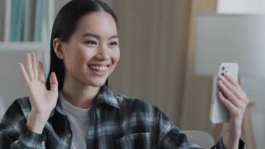 Mutlu Asyalı arkadaş canlısı blogger vlogger gülümseyen kadın cep telefonu videosu uzaktan iletişim selamlaması el sallayan akıllı telefon web kamerası sanal konuşma uygulaması çevrimiçi konuşma