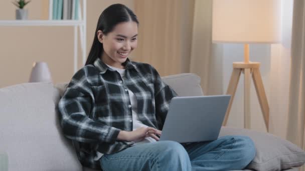 アジアの20代の女の子のユーザー100万人の女性の学生のフリーランス女性は、ラップトップの家のソファとインターネットでチャットコンピュータゲームをプレイ笑顔幸せなショッピングビデオ面白いソーシャルネットワークアプリを見て選択 — ストック動画