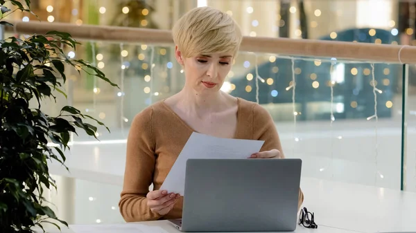 Caucasienne d'âge moyen femme d'affaires enseignante pigiste paperasse assis table avec ordinateur portable paperasse sentiment frustré en colère en raison d'une erreur dans les documents documents données incohérence finances incorrectes — Photo