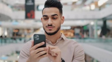 Mutlu gülümseyen Arap erkeği telefonu tutuyor. Neşeli adam piyango talihlisi, İspanyol asıllı, hızlı kredi için modern akıllı telefondaki bankacılık uygulamasını kullanarak başvuruyor.