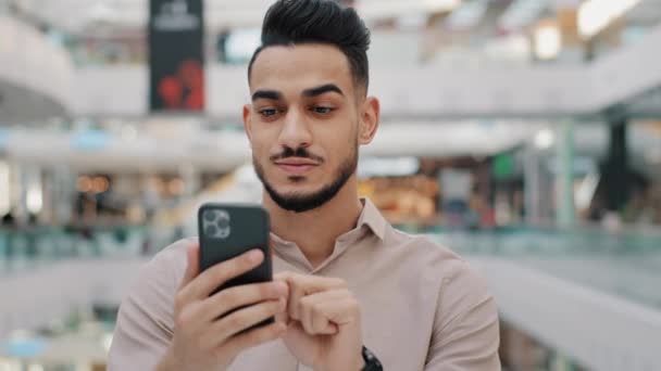 Mutlu gülümseyen Arap erkeği telefonu tutuyor. Neşeli adam piyango talihlisi, İspanyol asıllı, hızlı kredi için modern akıllı telefondaki bankacılık uygulamasını kullanarak başvuruyor. — Stok video