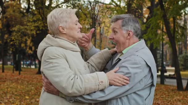 Радісна літня пара середнього віку обіймає сміючись стоячи в осінньому парку безтурботно спілкуючись щасливою усміхненою бабусею та дідусем, що приймає на відкритому повітрі святкування річниці весілля сімейні відносини — стокове відео