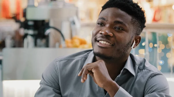Närbild ung glad afrikansk amerikansk man talar genom trådlösa hörlurar ler svara vänliga affärssamtal kommunicera förklara chatta med vänner på distans med hjälp av modern teknik — Stockfoto