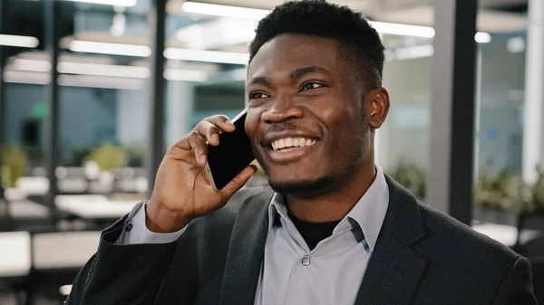 Afrikalı iş analisti, gülümseyen adam cep telefonuyla konuşuyor. Müşteri danışmanlığı yapıyor. Duygusal olarak kapalı alanda hikaye anlatıyor. — Stok fotoğraf