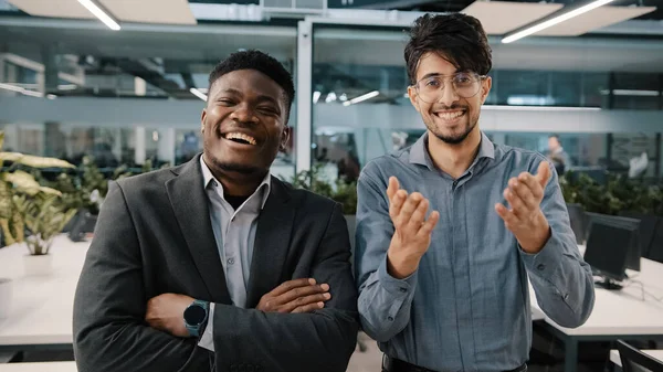 Twee vrolijke collega 's Afrikaanse man Arabische verkoper op zoek naar camera lachen grap grappige zakelijke situatie corporate grap in de werkruimte waarderen goed gevoel voor humor verheugen positieve sfeer — Stockfoto