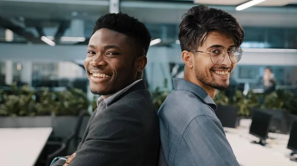 Portret van twee multinationale mannelijke collega 's Afrikaanse man Arabisch Indiase manager poseren in kantoor bedrijf staan terug naar elkaar partnerschap op zoek naar camera glimlachende zakenpartners werknemers — Stockfoto