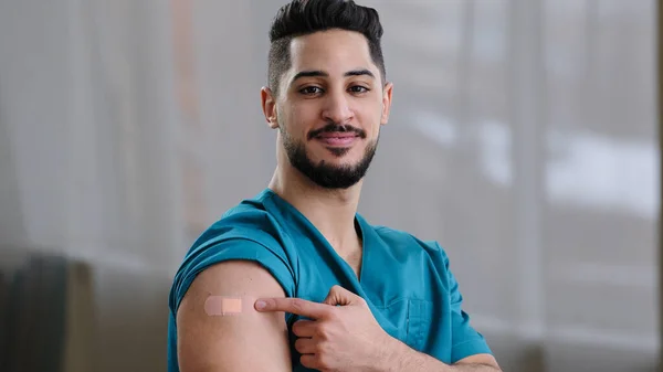 A covid-19 vírus emberéből beoltott ihletett arab férfi egészségügyi dolgozó, aki a vállon lévő injekció jelölésén lévő, a koronavírus-fertőzés immunitásvédelmét serkentő tapaszt mutató kamerát nézte — Stock Fotó