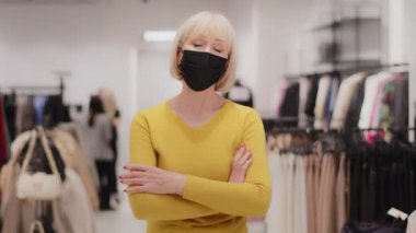 Başarılı orta yaşlı kadın satış danışmanı tıbbi maskeli mağaza sahibi güvenle kameraya bakıyor göğsünde çapraz duran küçük işletme konseptine bakıyor.