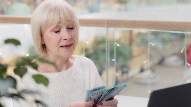 Successful middle aged woman sitting in office financial consultant bank employee communicates with client at distance via video conference using camera on laptop checks amount cash holds dollar bills — Stock Video